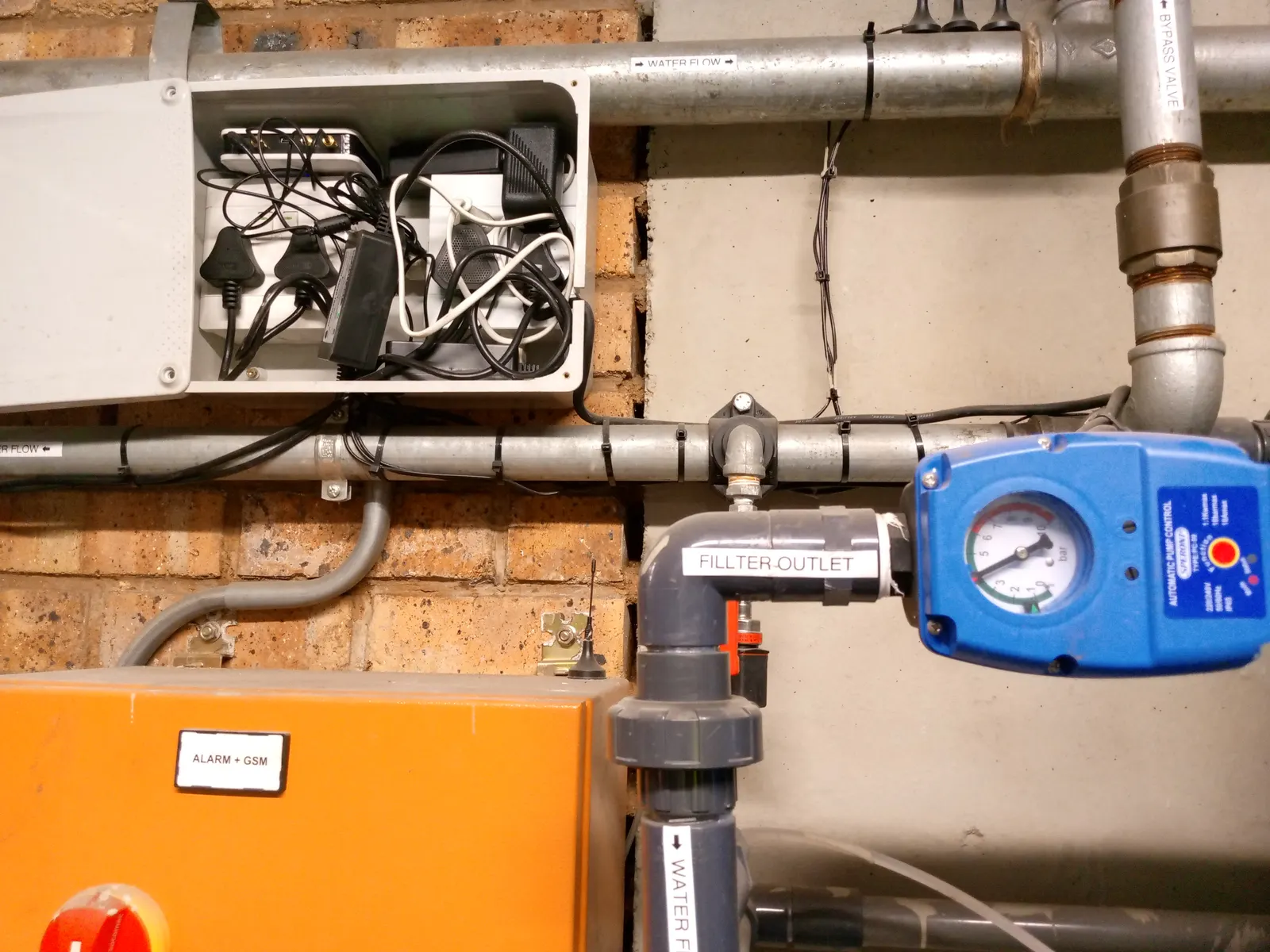 Plant room pipework with an actuated valve and pressure gauge on the outlet, alongside a control enclosure and cabling tray.