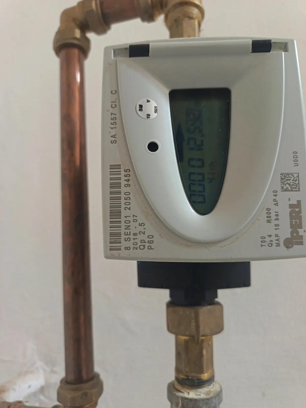 A water meter with a digital register installed inline on a copper riser.