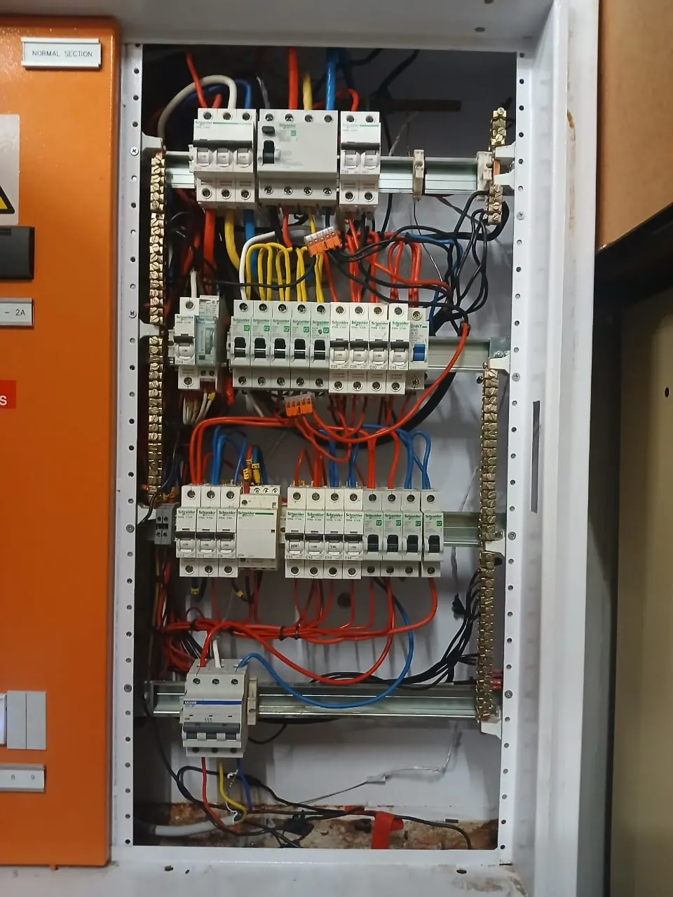 An open distribution board showing breakers on din rail, neutral and earth bars, and the incoming cabling dressed into the enclosure.
