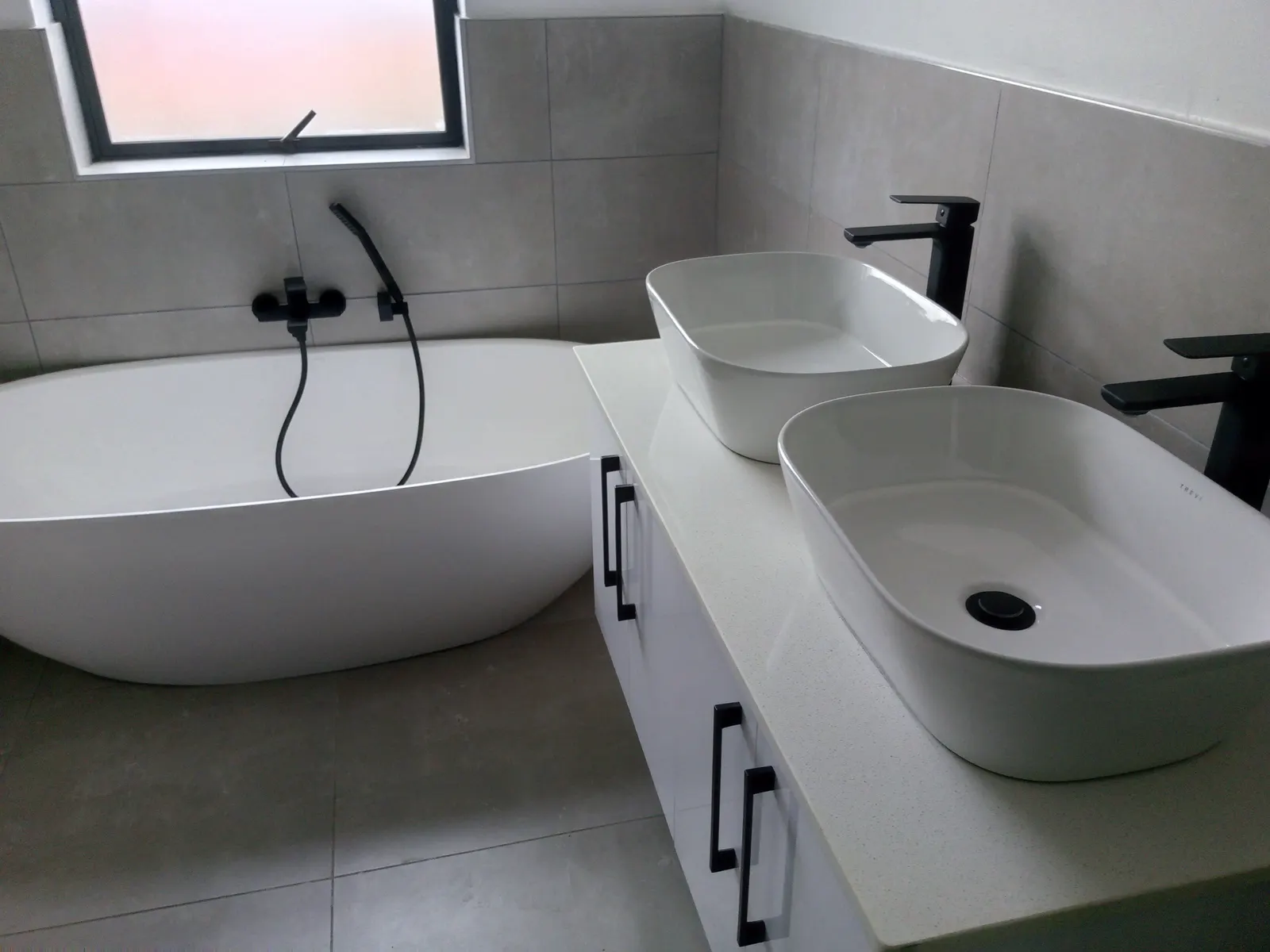 A finished bathroom with a freestanding bath, wall-mounted mixer and twin counter-top basins.