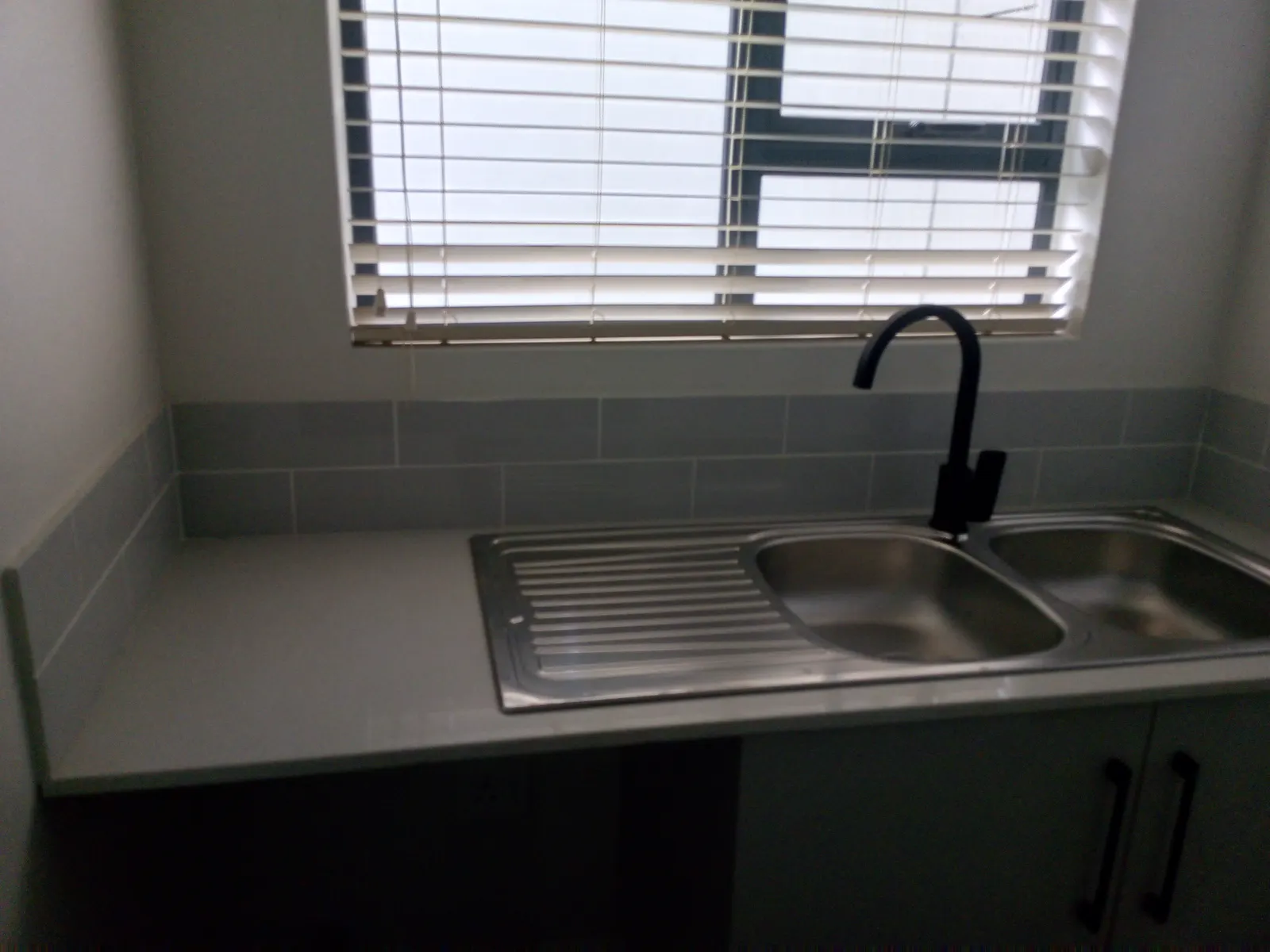 A completed kitchen installation with a double-bowl sink, mixer tap and tiled splashback under the window.