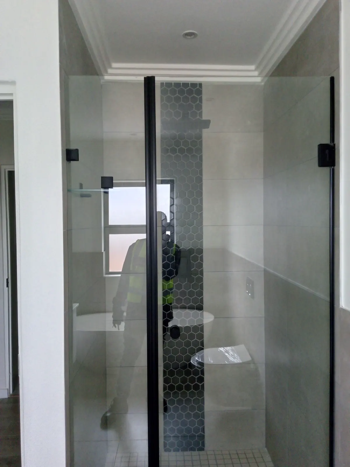 A frameless glass shower enclosure with a tiled feature band and recessed shelf.