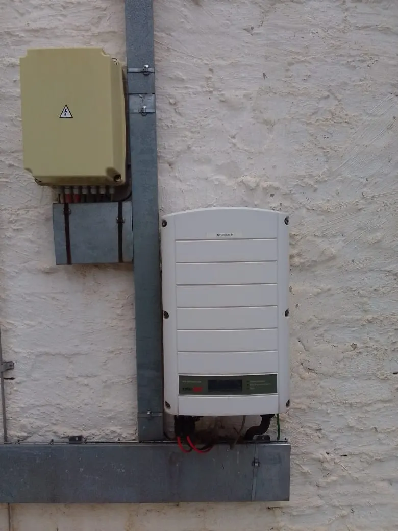 A wall-mounted string inverter beside an isolator enclosure, fed on galvanised channel up a plastered exterior wall.