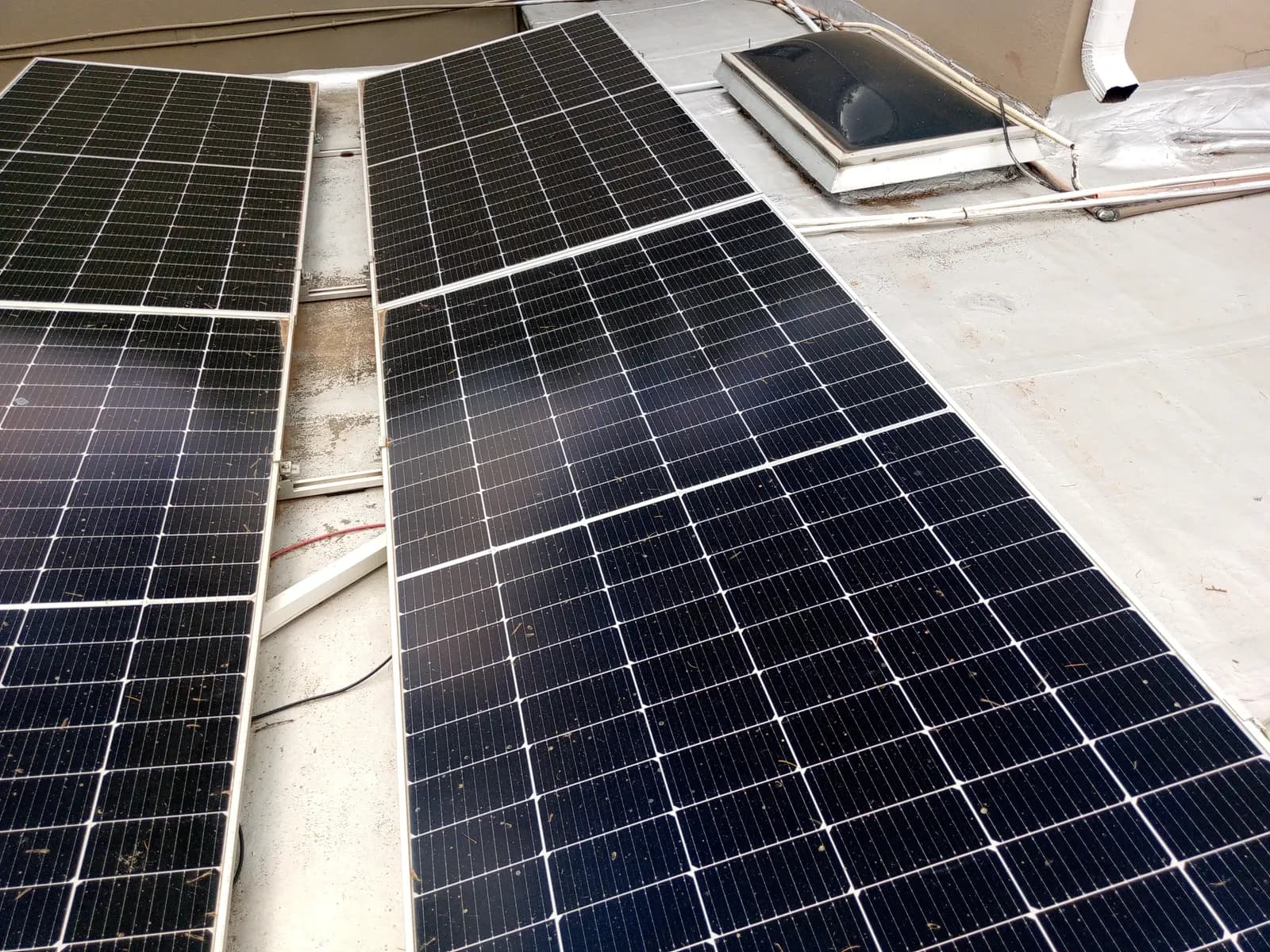 Close view of monocrystalline solar modules laid across a roof sheet, showing the mounting rail and cable run between rows.