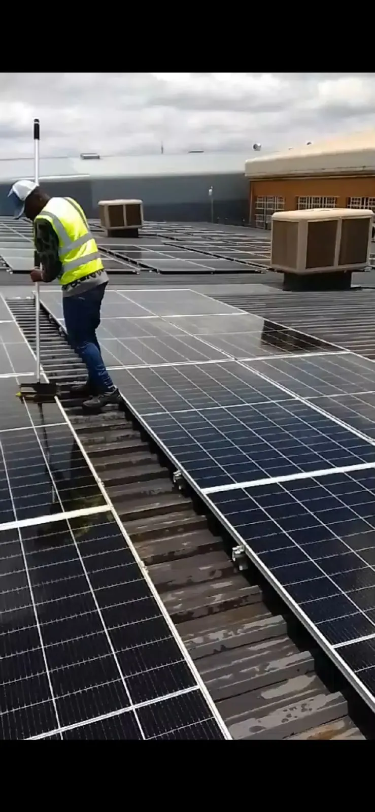 A technician in a hard hat and hi-vis vest setting panels into a rooftop mounting system.